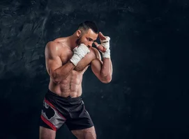 strong-muscular-fighter-is-showing-his-punch-while-posing-for-photographer-at-dark-photo-stud...webp